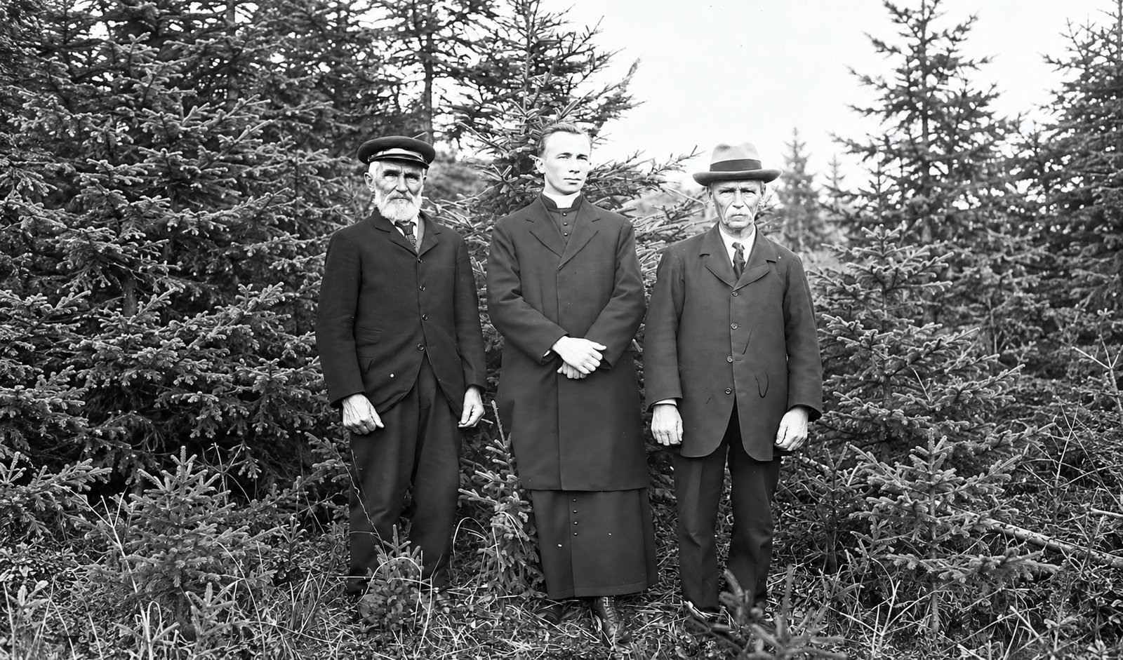 Mgr Labrie et deux hommes devant des conifères